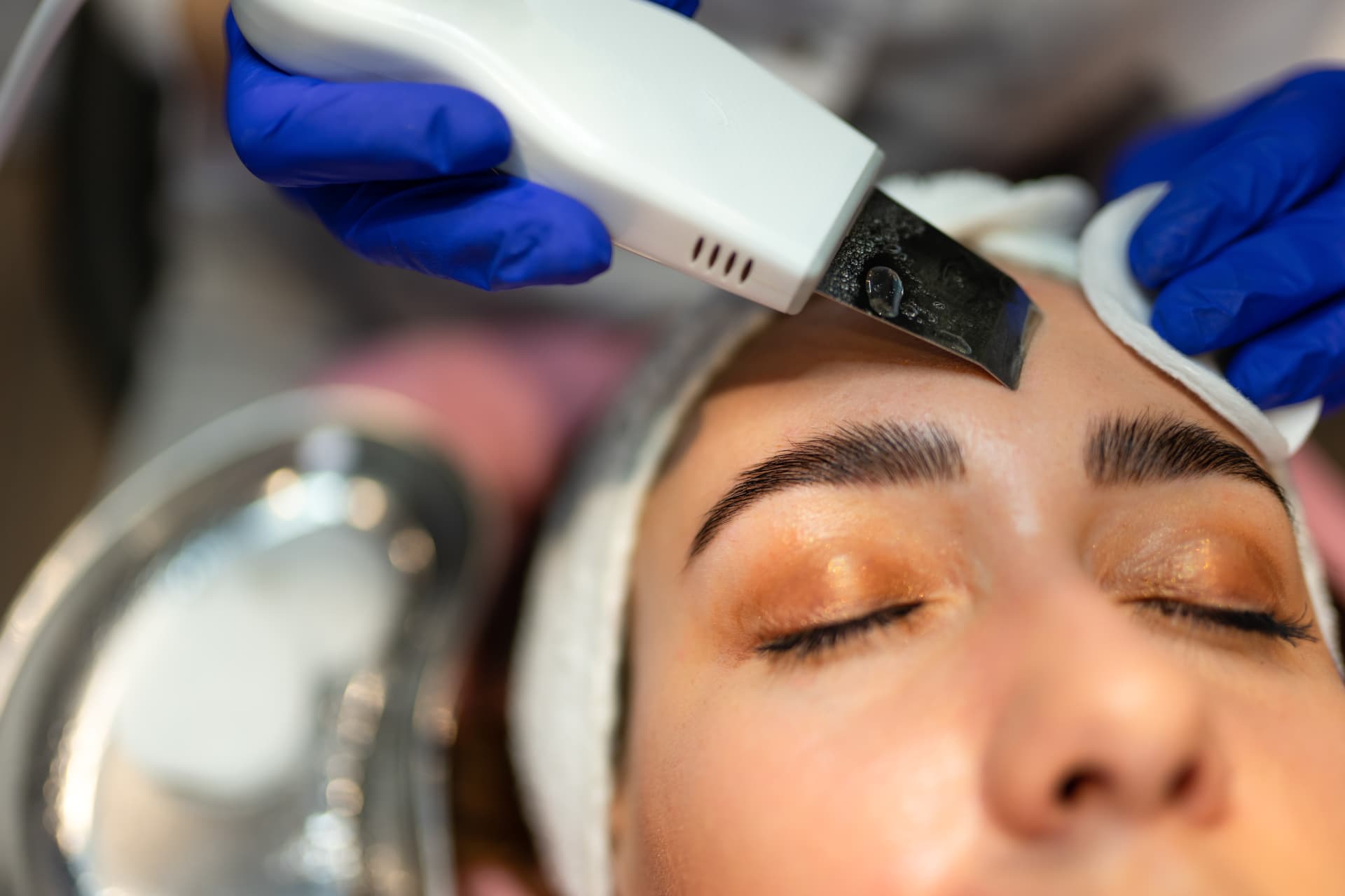 Esthetician performing a dermaplaning treatment on a client's forehead